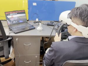A trainee in a VR headset at a steering wheel, driving the simulation in the HapzXR studio